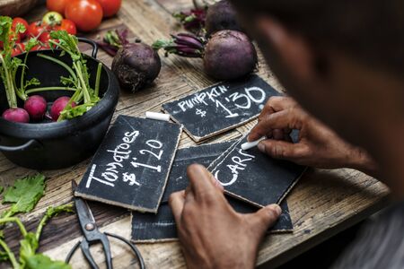 Rear view of man writing vegetable price on chalk board