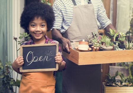 Man Carrying Plants Standing With Son Showing Open Sign