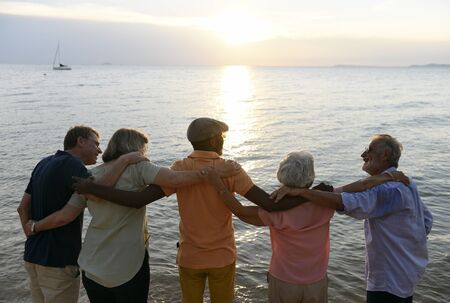Group of senior friends arm around on the beach