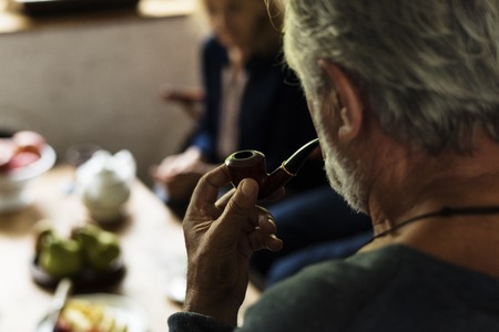A senior man smoking pipe while talking with his friend
