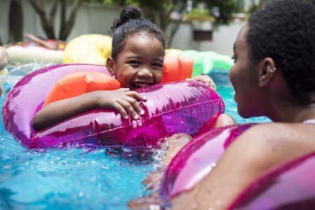 Closeup of black mother and daughter enjoying the pool with inflatable tubes
