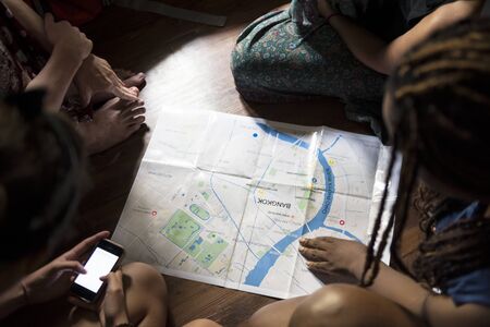 Group of diverse tourists sitting on the wooden floor planning checking on the map