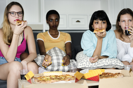 Diverse women sitting on the couch eating pizza together