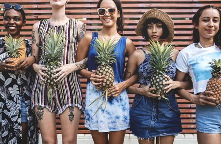 A diverse group of women standing and holding pineapple together
