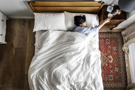 Asian woman on the bed waking up by the alarm clock