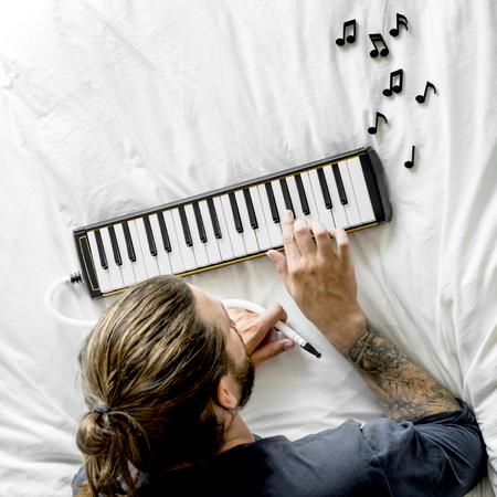 Man lying on bed and using a melodica