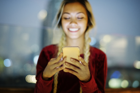 Smiling young woman using a smartphone in the evening cityscape