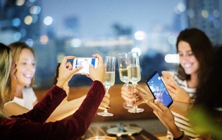 Girl friends having a dinner together at a rooftop bar taking a photo of the toast social media...