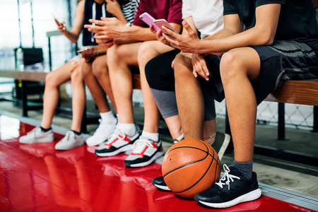 Group of young teenager friends on a basketball court relaxing using smartphone addiction concept
