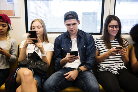 Group of young adult friends using smartphones in the subway