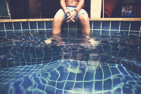Young caucasian boy put feet in swimming pool