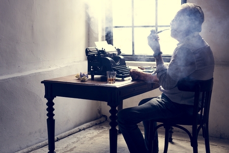 Elderly man sitting smoking pipe with retro typwriter on wooden table