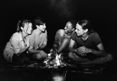 Group of young adult friends sitting around the bonfire outdoors recreational leisure and friendship...
