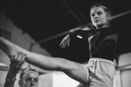 Coach training young gymnast to balance on a balance beam