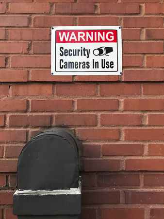 Warning security cameras in use sign on a brick wall