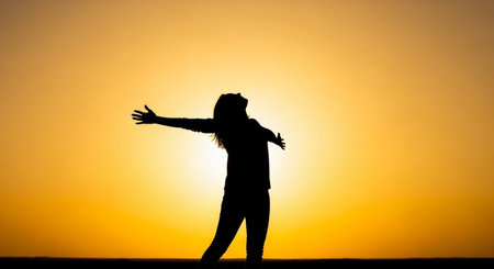 Silhouette of a woman raising her hands up at sunset.の素材
