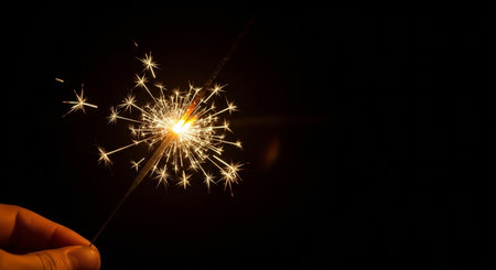 Christmas and New Year party sparkler in hand on black background with copy spaceの素材