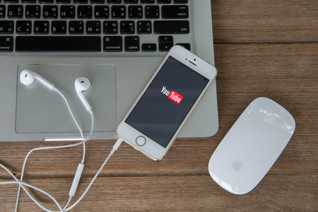 CHIANGMAI, THAILAND -June 22, 2015:Brand new Apple iPhone with YouTube app on the screen lying on desk with headphones.のeditorial素材