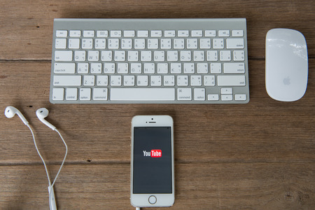 CHIANGMAI, THAILAND -June 22, 2015:Brand new Apple iPhone with YouTube app on the screen lying on desk with headphones.のeditorial素材