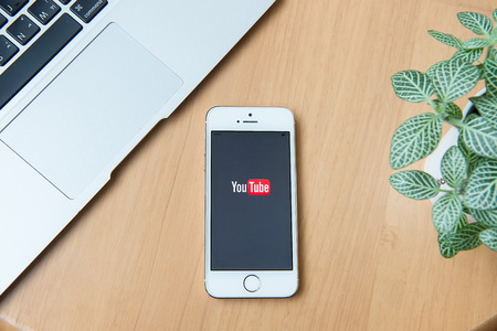 CHIANGMAI, THAILAND -June 24, 2015:Brand new Apple iPhone with YouTube app on the screen lying on desk with headphones.のeditorial素材