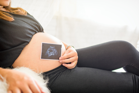 pregnant woman holding ultrasound scan on her tummywith copy space.の写真素材