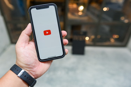 CHIANGMAI, THAILAND - JAN 08,2018 :Brand new Apple iphone X with YouTube app on the screen lying on old wood desk with headphones. YouTube is the popular online video sharing websiteのeditorial素材