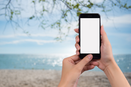 Young womanholding mobile smart phone and the background is the sea during the holiday seasonの写真素材