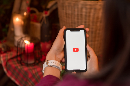 CHIANGMAI, THAILAND - JAN 16,2018 :Brand new Apple iphone X with YouTube app on the screen lying on old wood desk with headphones. YouTube is the popular online video sharing websiteのeditorial素材