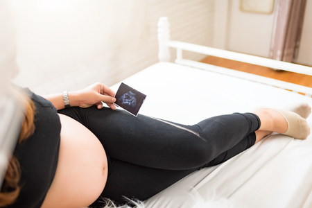 pregnant woman holding ultrasound scan on her tummywith copy space.
