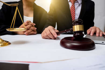 justice and law concept.Male judge in a courtroom with the gavel,working with,digital tablet computer docking keyboard,eyeglasses,on wood table warm colours sun light.の写真素材
