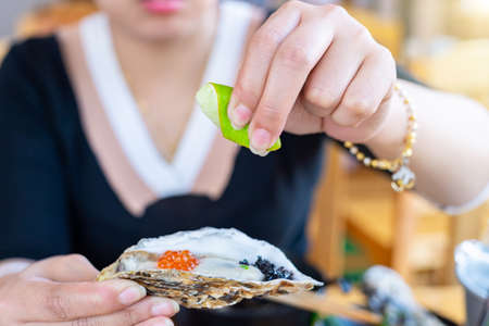Close up on hand of a woman squeezing a lemon into a large oyster in restaurant holding oysterの写真素材