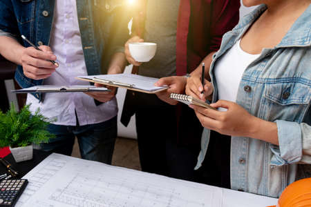 team colleagues discussing data working and tablet, laptop with on on architectural project at construction site at desk in office warm colours sun lightの写真素材