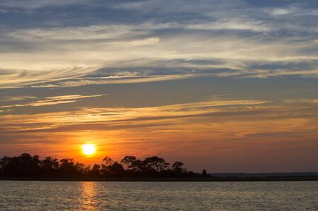 A colorful cloudy sky as the sun sets over water and trees.の写真素材