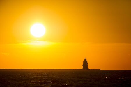 The sun rises behind a silhoetted lighthouse in the Atlantic Ocean.の写真素材