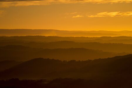 Layers of mountains fade into the distance in the glowing sunrise orange light.