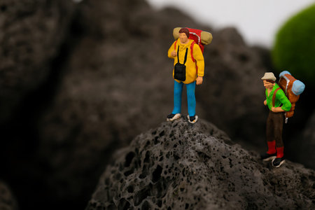 Miniature people : Traveler with backpack standing on the rock.