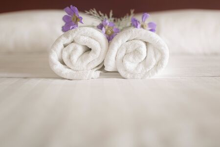 Closeup of a set of white towel rolls on a hotel bed with purple flowers on themの写真素材