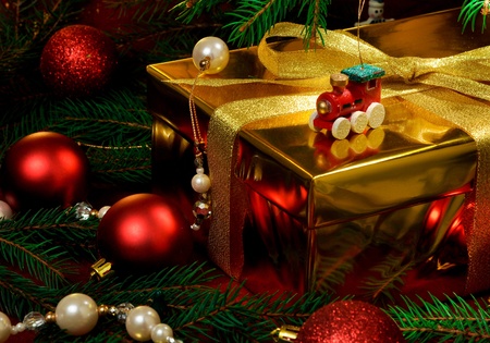 a gold box tied with gold ribbon surrounded by red christmas toys and christmas treeの写真素材