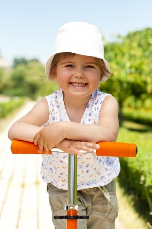 Little adorable girl posing with orange scooter in the parkの写真素材