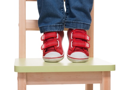 child's feet standing on the little chair on tiptoes on white backgroundの写真素材