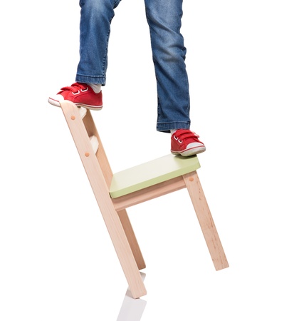 child's feet standing on the little chair on white backgroundの写真素材