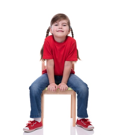 little girl wearing red t-shirt and posing on chair isolated on whiteの写真素材