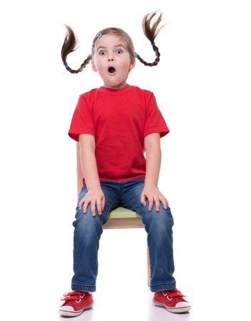 very surprised little girl with funny pigtails wearing red t-short and sitting on the chair isolated on whiteの写真素材