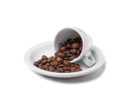 little cup with scattered coffee beans lying on saucer on white backgroundの写真素材