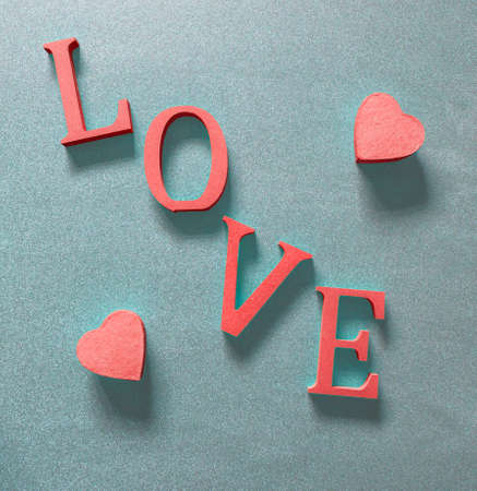 two pink hearts either side of the word love in red on a textured blue grey background from above