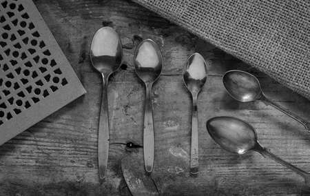 close up macro collection of vintage silver spoons on a rustic background from above photographed in black and whiteの写真素材