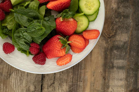 a close up of a mix of berries and salad vegetables on a white plate on a rustic background from above copy spaceの写真素材