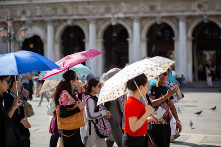 showing the crowds of tourists with umbrellas and parasols that congest the city streets who go to look at the famous Venetian landmarks every yearのeditorial素材