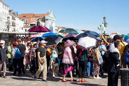 showing the crowds of tourists with umbrellas and parasols that congest the city streets who go to...