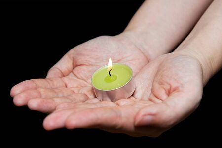 Burning candle in female hands isolated on blackの写真素材